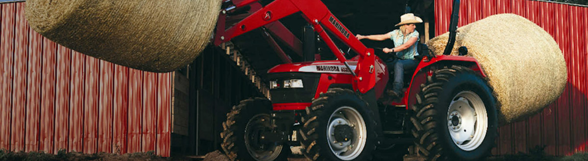 Woman riding a red Mahindra tractor picking up hay bales
